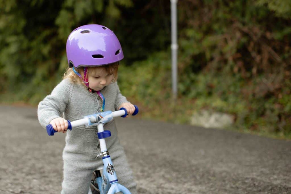 Bicycle Helmet Laws by US States - This image is shows a baby girl riding her bicycle and wearing a pink helmet fitted and strapped to her head.