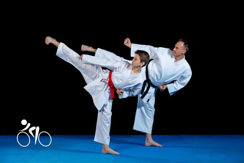 Phot of two people practicing Karate. An older person black belt and a young kid red belt on a blue tatami and a black background.