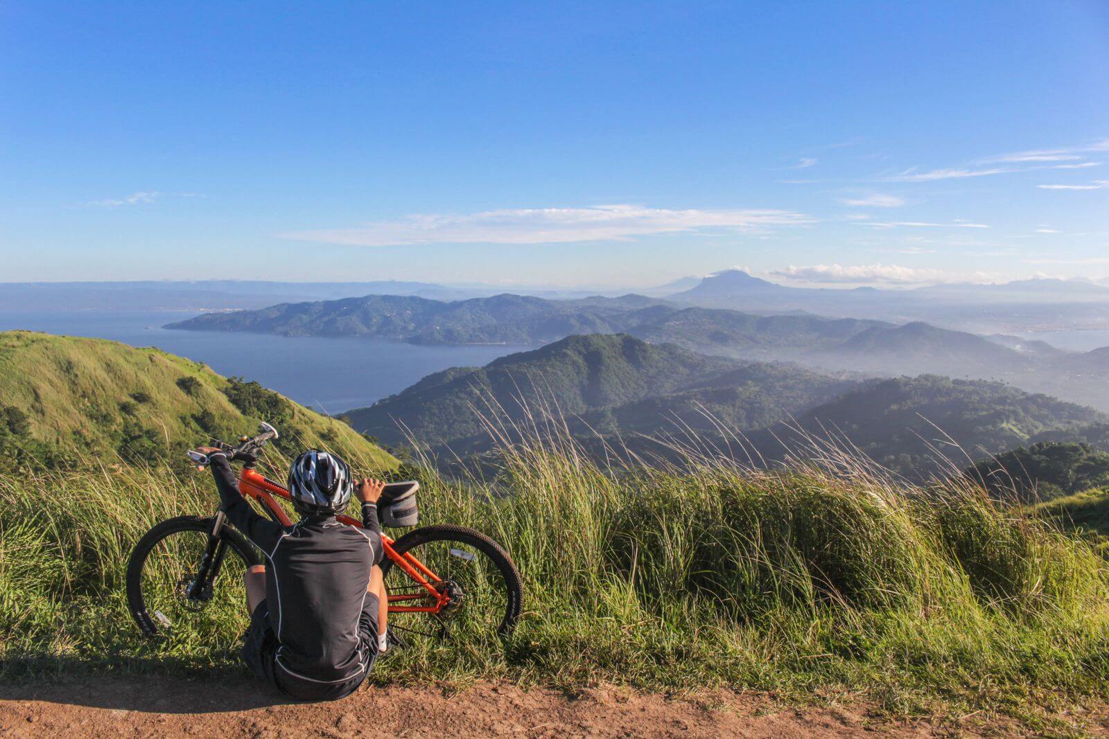 Cyclist with his bike resting sitting on the ground looking the view.